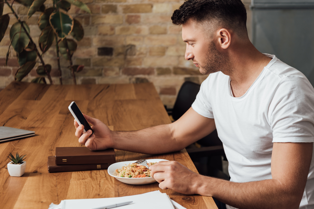 Muškarac ruča uz mobitel